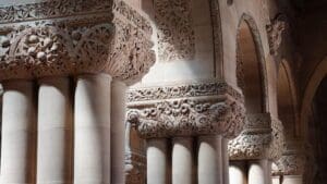 Intricately carved stone columns and arches with detailed floral and geometric patterns, illuminated by soft, natural light. The architecture is ornate and historical, conveying a sense of grandeur and artistry.