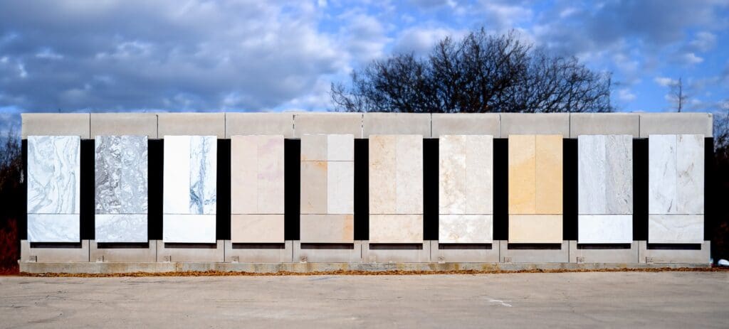 A series of rectangular stone panels is displayed outdoors against a backdrop of trees and a cloudy sky, reminiscent of the dignified architecture planned for the Obama Presidential Center. The panels vary in shades of gray, beige, and white, arranged in a uniform vertical sequence.