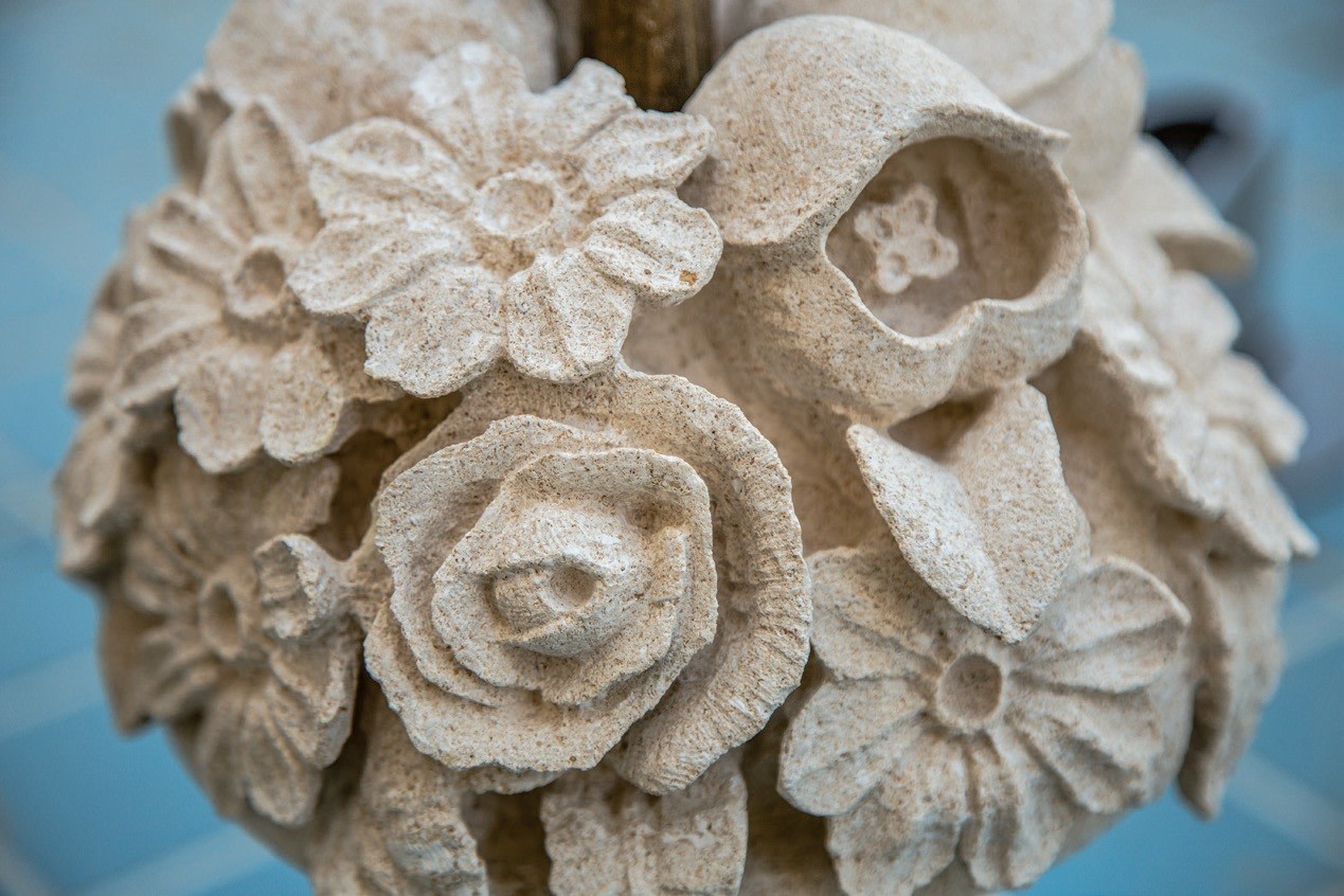 Close-up of an intricate stone sculpture at Longwood Gardens, featuring various flowers such as roses and lilies. The detailed petals and textures reflect the artistry found in horticulture. A slightly blurred blue surface enhances the captivating scene.