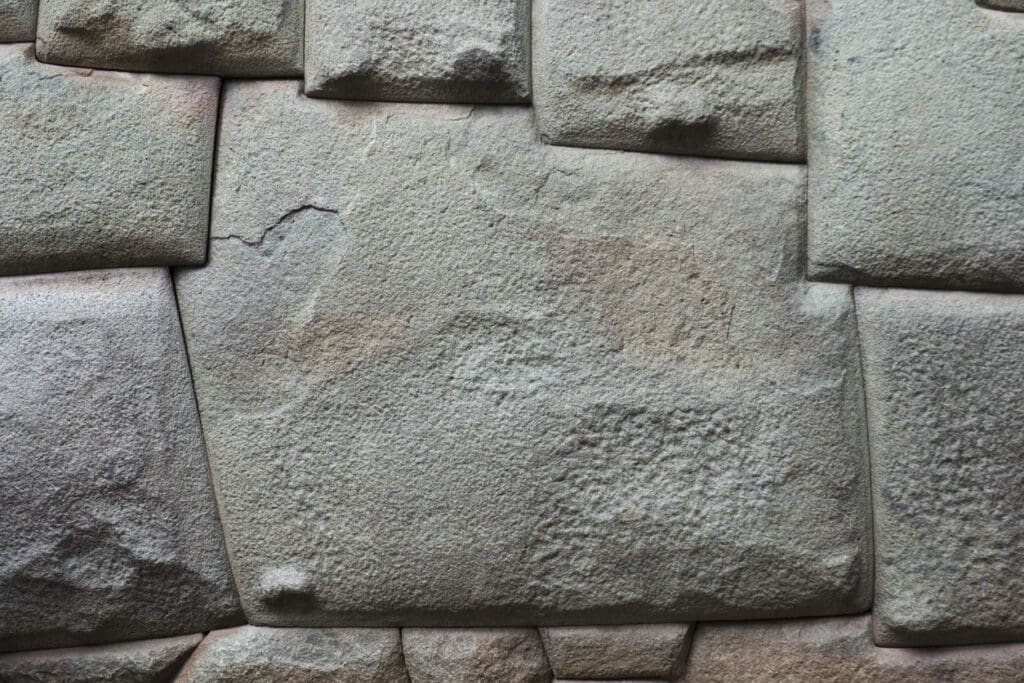 Close-up of an ancient stone wall showcasing timeless beauty with precisely cut, interlocking natural stone blocks. The gray stones have smooth surfaces and varying shades, showing signs of wear and age, fitting together seamlessly without visible mortar—a testament to remarkable architecture.