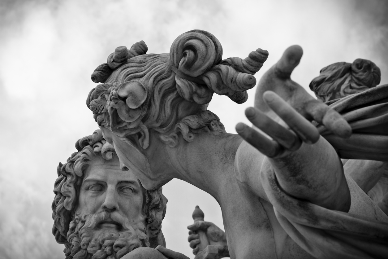 Close-up of a dramatic white marble sculpture featuring two figures; one with curly hair and a beard, the other with flowing hair and an outstretched arm, set against a cloudy sky.