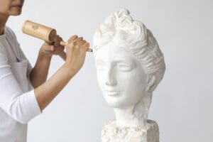 Artist carving a white marble bust sculpture by hand, showcasing traditional marble stone carving techniques and classical fine art craftsmanship.
