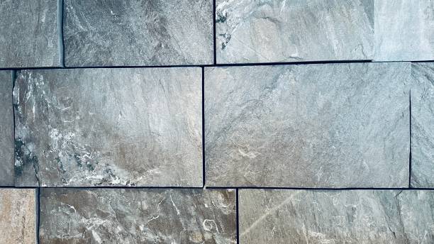 Close-up of a stone wall with large, rectangular gray slate tiles, reminiscent of Peter Zumthor’s use of architectural stone. The rough, natural texture showcases subtle variations in Swiss stone, and the grout lines between the stones are thin and even.