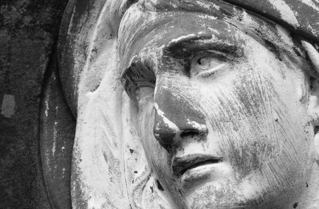 Close-up of a weathered stone statue’s face, its textured features and streaks of erosion hinting at the need for best stone preservation practices. Deep shadows emphasize the eyes and mouth, highlighting times impact on long-term longevity.