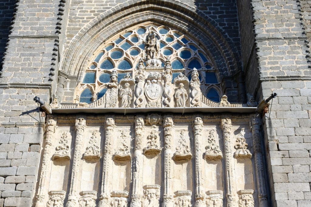 Ornate stone facade of a gothic cathedral with arched stained glass window and detailed sculptures above the entrance. Sunlight highlights intricate carvings and textures, reminiscent of Swiss stone craftsmanship and Peter Zumthor’s architectural finesse.