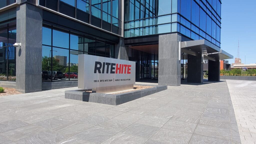 A modern glass office building serves as the Rite-Hite Global Headquarters, with a large sign reading RITEHITE in bold letters and the address 195 S. RITE-HITE Way, set along a paved walkway.
