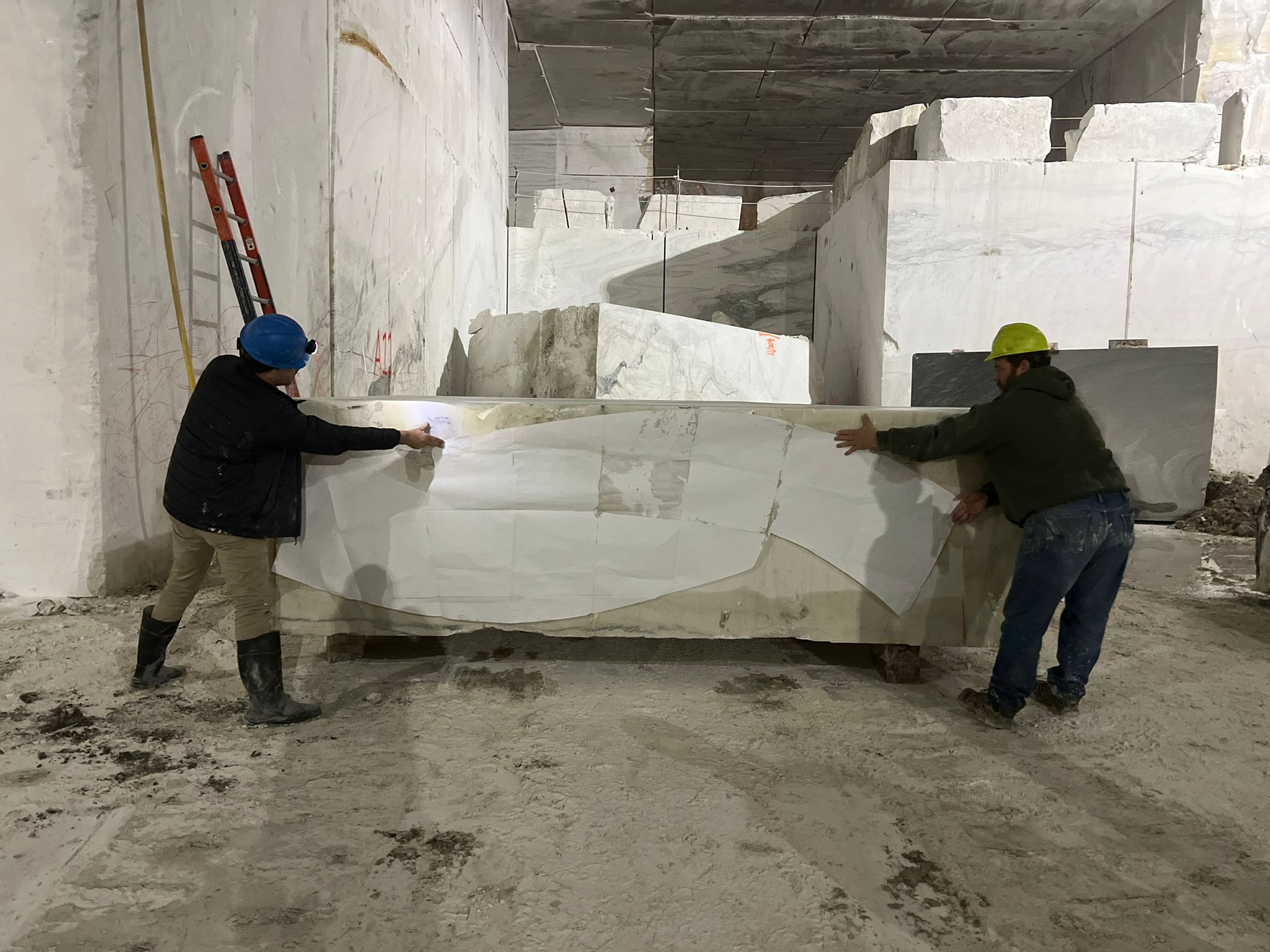 During a site visit at the Vermont Marble Quarry, two people wearing hard hats hold a large sheet of paper against a stone slab, surrounded by marble blocks and construction equipment for the E9 Project Assessment.