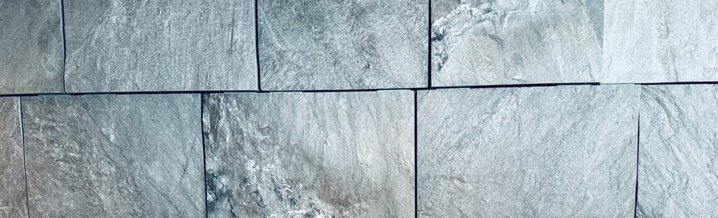 Close-up of a wall made of rectangular stone tiles in shades of gray and blue, with visible natural texture and slight gaps between some tiles.